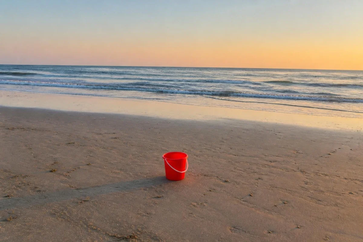 AI-generated photo of a beach at sunset with a red bucket on the sand